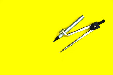 Single compass attached to a silver color wood pencil crayon on a yellow background