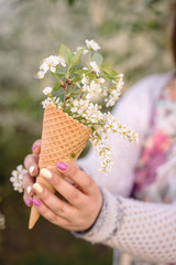 Beautiful waffle cone with ice cream decorated with flowers in the girl&rsquo;s hand with multi-colored bright manicure