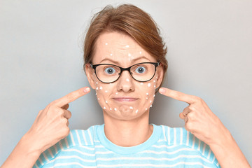 Portrait of cute puzzled girl with white drops of face cream on skin