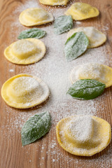 Aerial view of mushroom ravioli and basil, with flour falling, on wooden table, vertical