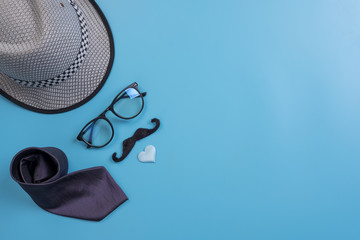 Happy Fathers Day background concept.Decorated hat, eyeglasses,  necktie, mustache light blue heart on light blue pastel background with copy space. Top view, flat lay.