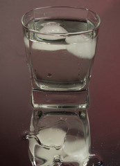 Bartender pouring up frozen vodka from a bottle into two shots glasses with ice cubes against black background. Barman pour of clear transparent alcohol drink rum tequila in shot-glass