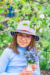 girl in a hat with blue flowers in the summer garden