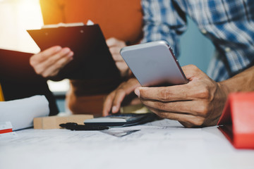 group of engineer and architect working on digital mobile phone and blueprint on workplace desk in meeting room project at construction site office, contractor, engineering and construction concept