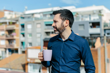 Relaxing moment of a middle-aged man standing on the balcony drinking coffee