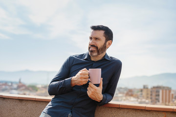 Relaxing moment of a middle-aged man standing on the balcony drinking coffee