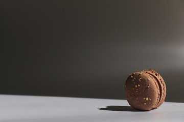 One cake of brown chocolate macaron or macaroon with shadow from window. Delicious macaroon isolated on white and gray background. French sweet cookie.
