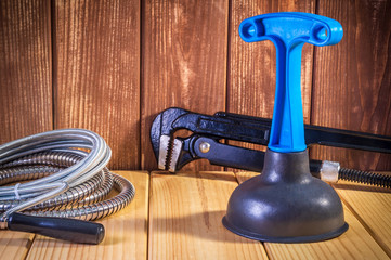 Clean plastic plunger with blue handle, pipe wrench and cable on wooden background.
