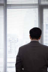 Back View of Asian Businessman in a Suit Looking Through Office Window with Blank Copyspace