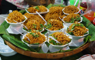 Asian noodle in white bowls with plastic forks selling on traditional market.