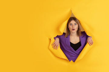 Wondered, shocked. Cheerful caucasian young woman poses in torn yellow paper background, emotional and expressive. Breaking on, breakthrought. Concept of human emotions, facial expression, sales, ad.