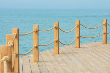 Naklejka premium Wooden platform on the seashore. Wooden poles connected by ropes are placed around the perimeter of the site. Beautiful view of the calm sea.
