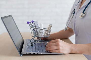 Unrecognizable woman doctor on online consultation for laptop. Online pharmacy concept. Faceless pharmacist puts medicine in a mini shopping cart.
