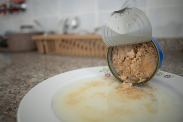 Fototapeta premium Canned tuna in a porcelain plate and on the kitchen counter. Spilled on the plate. Close up.