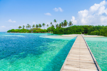 Wooden bridge over turquoise water to a tropical island in the Maldives