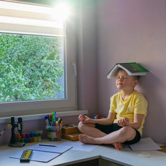 blonde boy sitting in yoga pose on a table with a book on his head