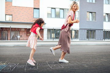 Outdoor image of happy little girl playing hopscotch with her mother on playground outdoors. Child...