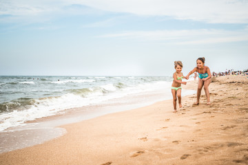 Two positive little girls run along the sandy beach on a sunny warm summer day. The concept of active child rest and children's health. Copyspace