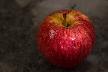 Juicy fresh red apple with water droplets on a dark background with space for text.