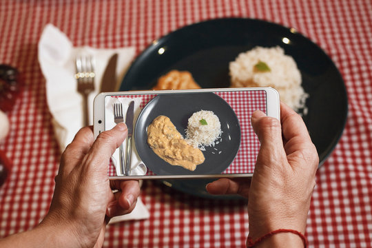 woman taking a picture with her cell phone to a plate of chicken strogononoff