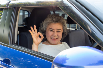 Asian senior woman driving a car showing ok with glad positive expression during the drive to travel journey, People enjoy laughing transport and drive thru concept