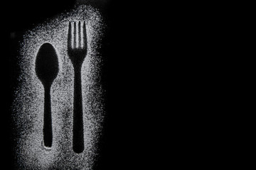 Fork and tea spoon silhouette made with flour on black background, up horizontal view with free...