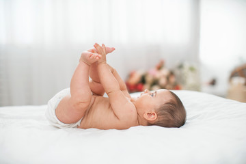 Cute baby is lying on his back on the bed and playing with his arms and legs