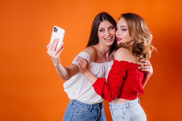 Two young and beautiful girls take a selfie and watch the phone in the Studio on a purple background. Girls for advertising