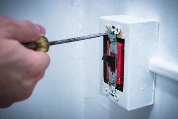 Man's hand using screwdriver to replace/repair 20 amp lightswitch on wall.
