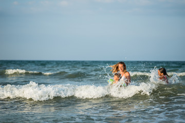 Cheerful young mother swims in the sea with her charming little daughters and enjoy the long-awaited weekend on a sunny summer day. Concept family vacation.