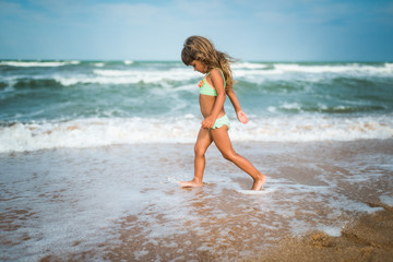 Fototapeta na wymiar Joyful little girl enjoys a beach day while relaxing at sea on a sunny warm summer day. Summer vacation and relaxation concept
