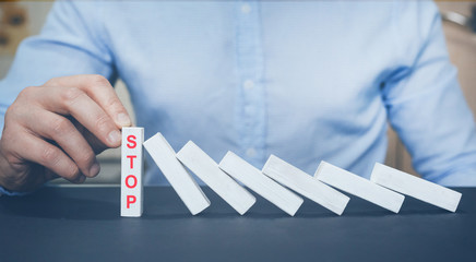 Businessman hand trying to stop dominoes. Risk management and insurance concept. Bankruptcy,...