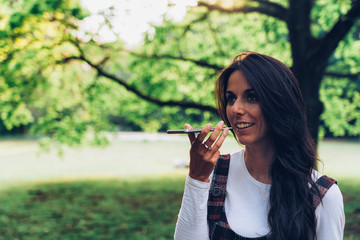 Fototapeta premium Young woman speaking a voice message on a mobile phone