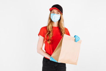 Courier in uniform, with a medical mask on his face and gloves holding a paper bag with food on a white background. The concept of shipping, quarantine, coronavirus