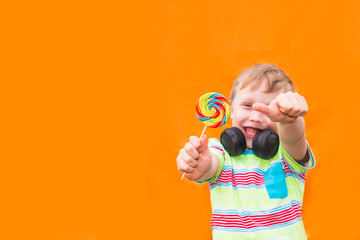 Boy child European with a colorful Lollipop on a stick on an orange background. The kid smiles and gives a thumbs up.