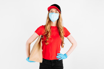 Fototapeta na wymiar Courier in uniform, with a medical mask on his face and gloves holding a paper bag with food on a white background. The concept of shipping, quarantine, coronavirus
