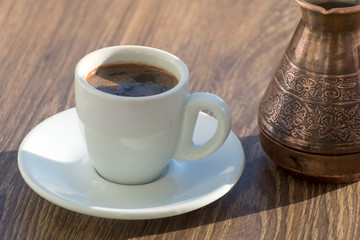 A cup of black coffee in a turk is on the table. Drinking coffee in the early morning.