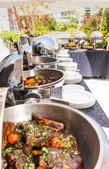 Live food stations in the line. Buffet Table with Row of Food Service Steam Pans, grilled meat and chops