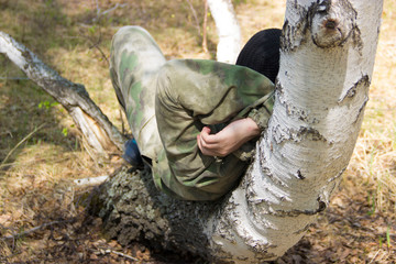 
A man in camouflage clothing is resting on a curved birch.