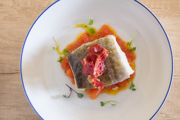Cenital plane of a fish dish, cod with tomato, served on a rustic plate, on wooden surface