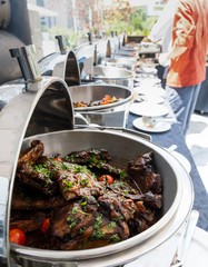 Live food stations in the line. Buffet Table with Row of Food Service Steam Pans, grilled meat and...