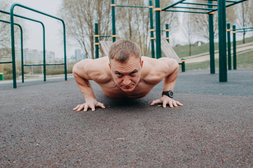 Young fit man doing push ups in a gym, Concentrated strong young bearded man in sportswear doing one armed push up on outdoor workout ground