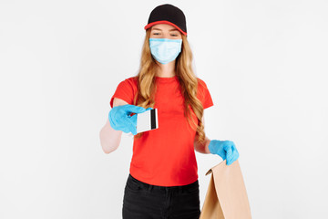 A courier, wearing medical rubber gloves and a medical mask, standing with a paper bag and a credit card on a white background. Online stores, payment by Bank transfer, quarantine, coronavirus
