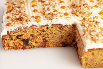 Slice of cake with white cream, caramel spots and nuts on white background