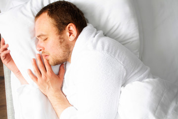A man sleeps in a white bed top view. Photo of a sleeping handsome man. Male dream.