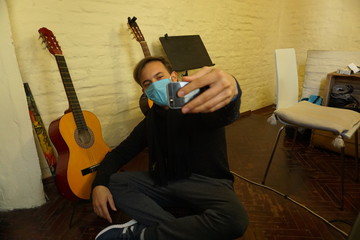 Hombre tom&aacute;ndose una selfie con barbijo en su casa con instrumentos de fondo