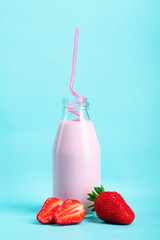 Milkshake with strawberries or drinking yogurt in a bottle with a beautiful straw with ripe strawberries and strawberry slices on a plain blue background.Healthy products from an organic farm