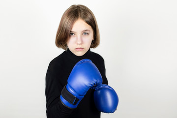 Teenage girl in boxing gloves on a light background. The girl has a serious face because she is preparing for the first competitions in her life