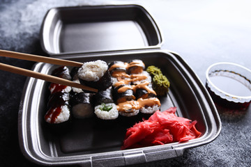 Set of delicious sushi rolls with wassabi and ginger in a box. Sushi rolls hold with wooden chopsticks. Soy sauce on a dark background. Japanese food.