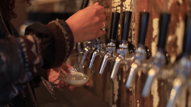 Selective focus of female bartender hands holding and filling glass of alcohol from wine wending machine while standing behind counter in a bar
